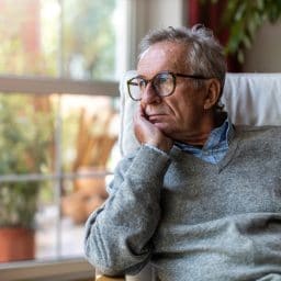 Older man looking out window of home.