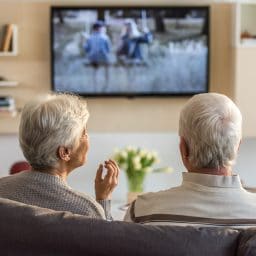 Older husband and wife sitting on the couch watching TV.