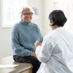 Older woman sitting on an exam table and talking with her doctor.