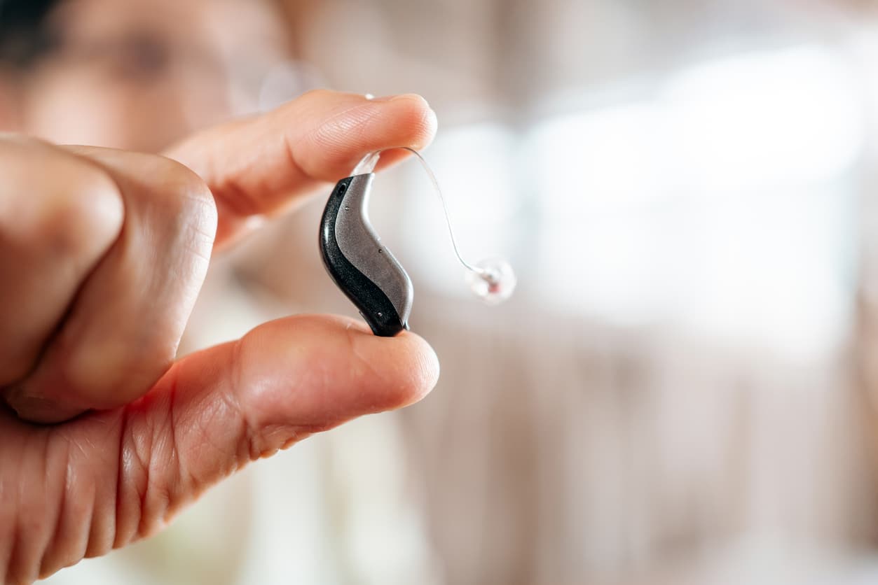 Close-up of a senior hand holding a modern hearing aid device.