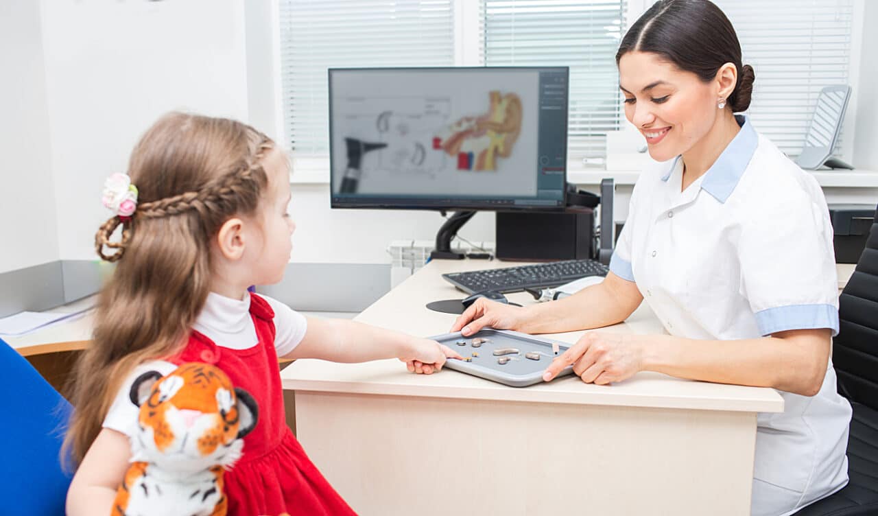 Little girl patient of a hearing clinic, chooses a hearing aid in an audiologist office. 