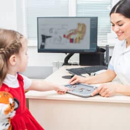 Little girl patient of a hearing clinic, chooses a hearing aid in an audiologist office.