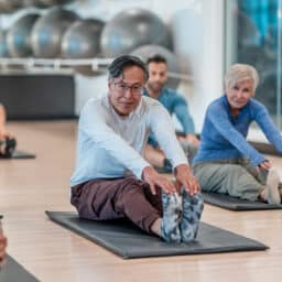 Group of adults participate in a fitness class, stretching on mats.