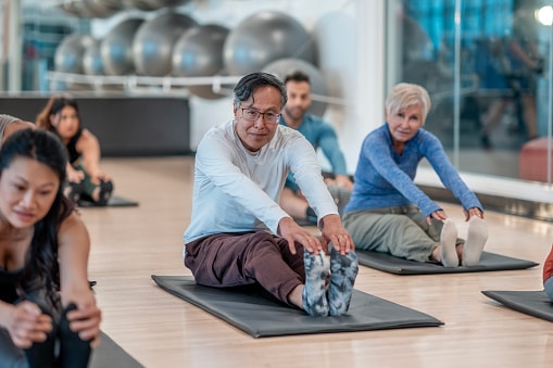 Group of adults participate in a fitness class, stretching on mats.