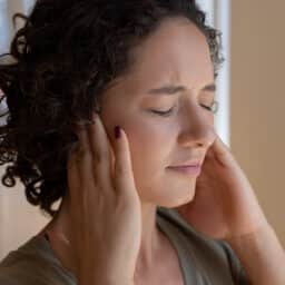 Woman covering her ears, trying to block out tinnitus.